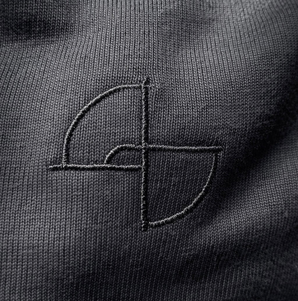 Close-up of subtle black embroidery on 215 gsm organic cotton T-shirt, ARC Exhibit 01 Vector
